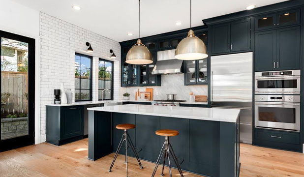 Stylish kitchen featuring navy blue cabinets, white countertops, stainless steel appliances, pendant lights, and wooden bar stools.