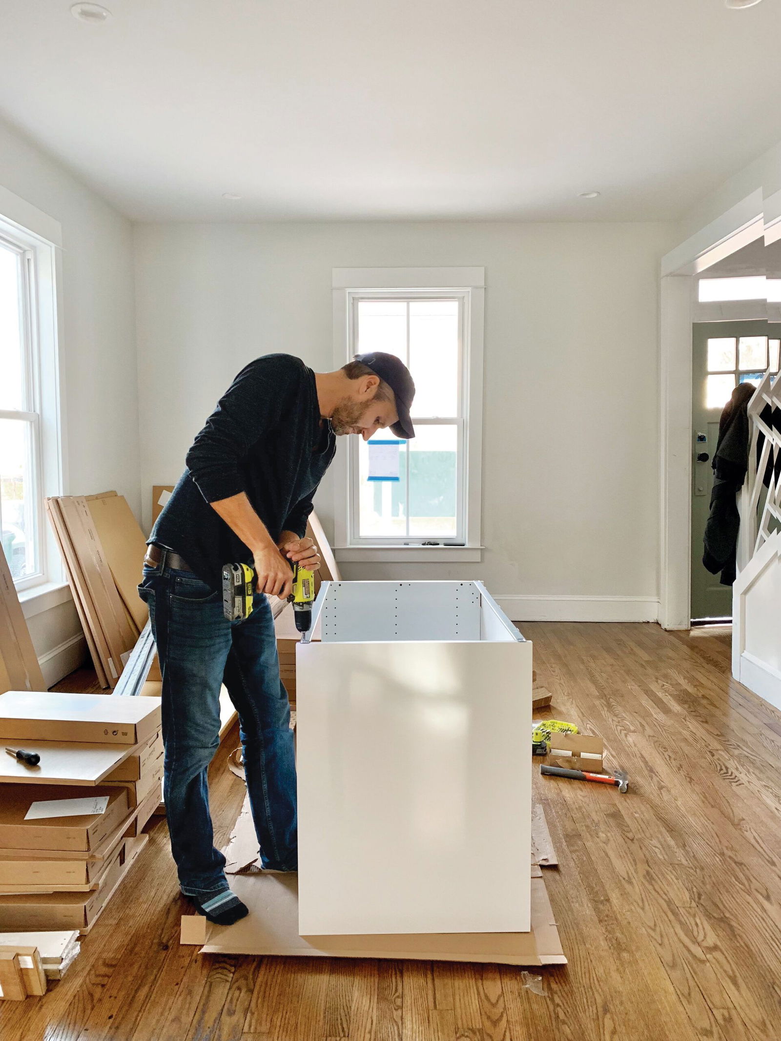Custom Closet Systems Personalized Guide 9 A man assembling a white kitchen cabinet using a power drill in a bright, modern home with hardwood flooring and natural light.