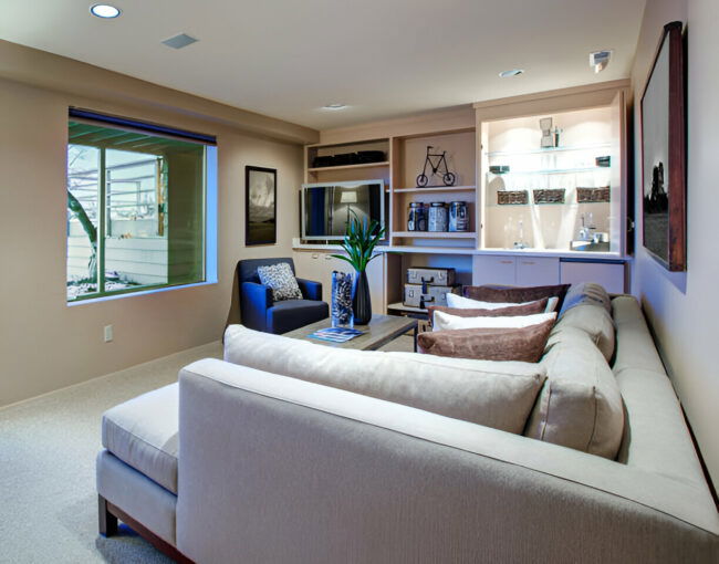 Modern basement living room with a sectional sofa, built-in shelves, and a small bar area
