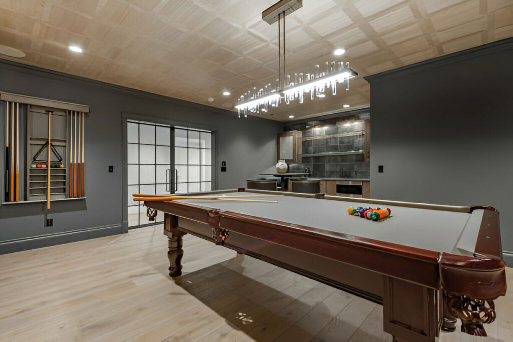 20 Inspiring Small Garage Conversion Ideas 19 Modern game room featuring a classic pool table, sleek gray walls, a built-in bar area, and a stylish chandelier