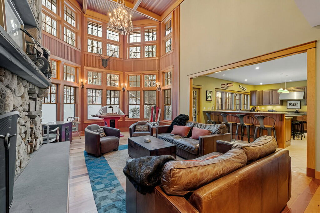 Spacious living room featuring high ceilings, large windows, cozy furniture, and an open view to a modern kitchen