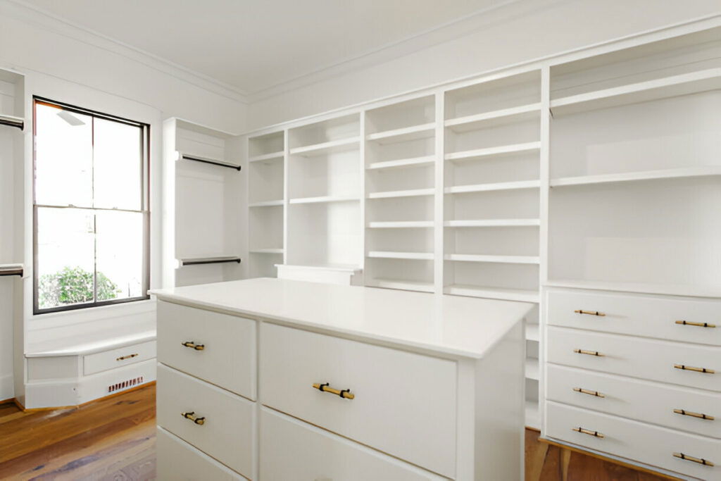 Modern white walk-in closet featuring ample shelving, storage drawers, and natural lighting from a large window
