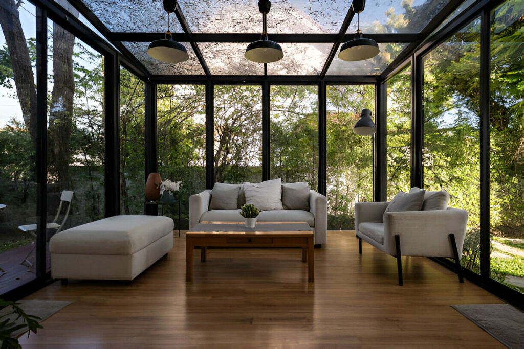 Elegant sunroom featuring glass walls and ceiling, contemporary seating, and abundant greenery views