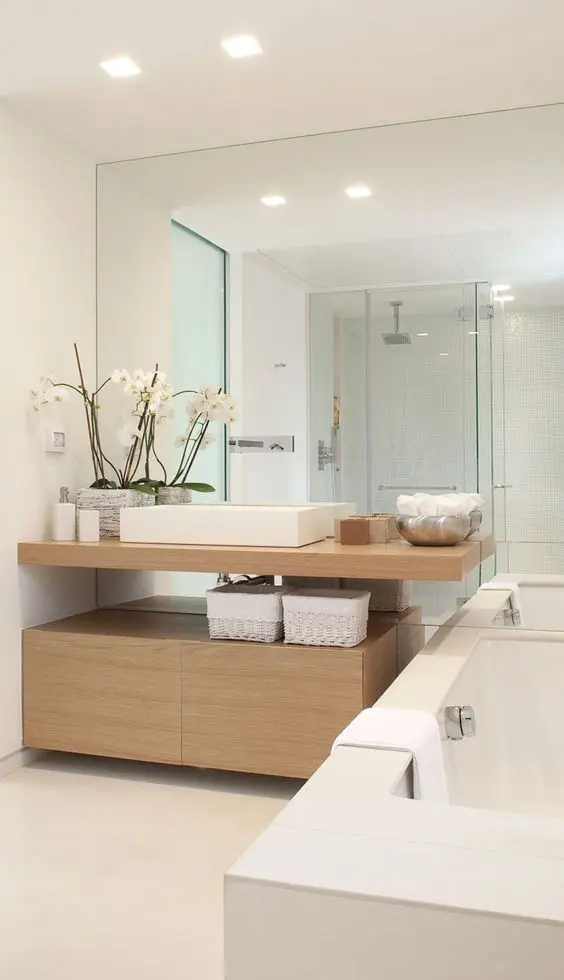 Minimalist modern bathroom with light wood vanity, large mirror wall, and clean white finishes.