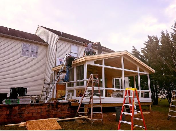 Workers building a sunroom addition with large glass panels and a pitched roof