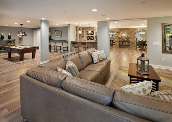 Finished basement with sectional sofa, bar area, pool table, and dining space featuring warm lighting and wood flooring.
