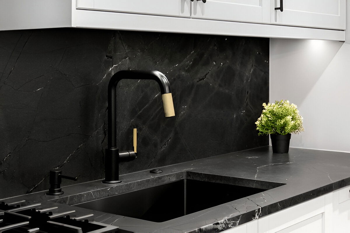 Modern kitchen with black marble backsplash and countertop, matte black sink and faucet with gold accents, and white shaker cabinets.