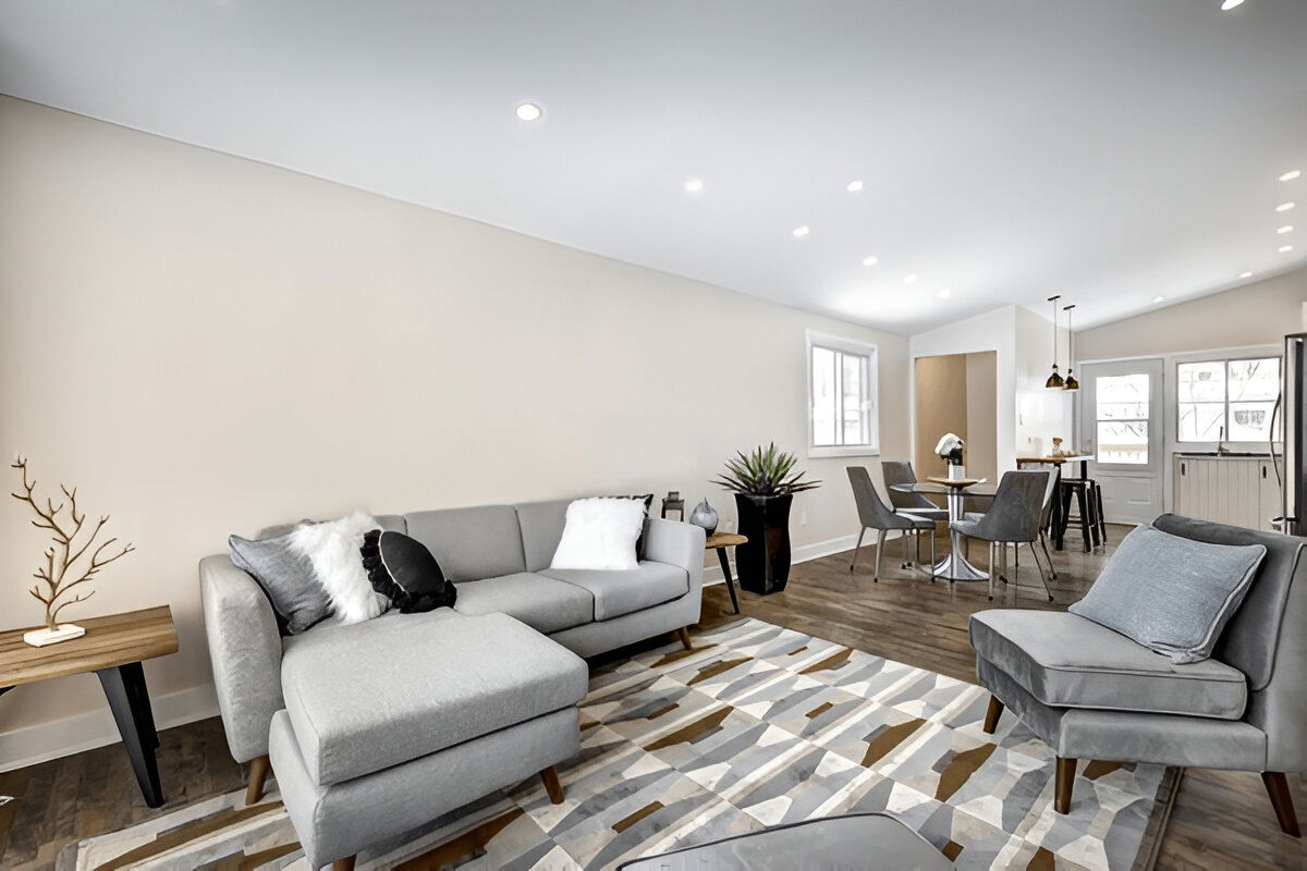 Modern open-plan living room and dining area with light gray furniture, neutral tones, wood floors, and minimalistic decor.