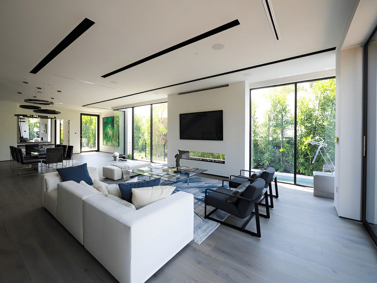 Spacious modern living and dining area with large windows, white sectional sofa, black chairs, and minimalist decor.