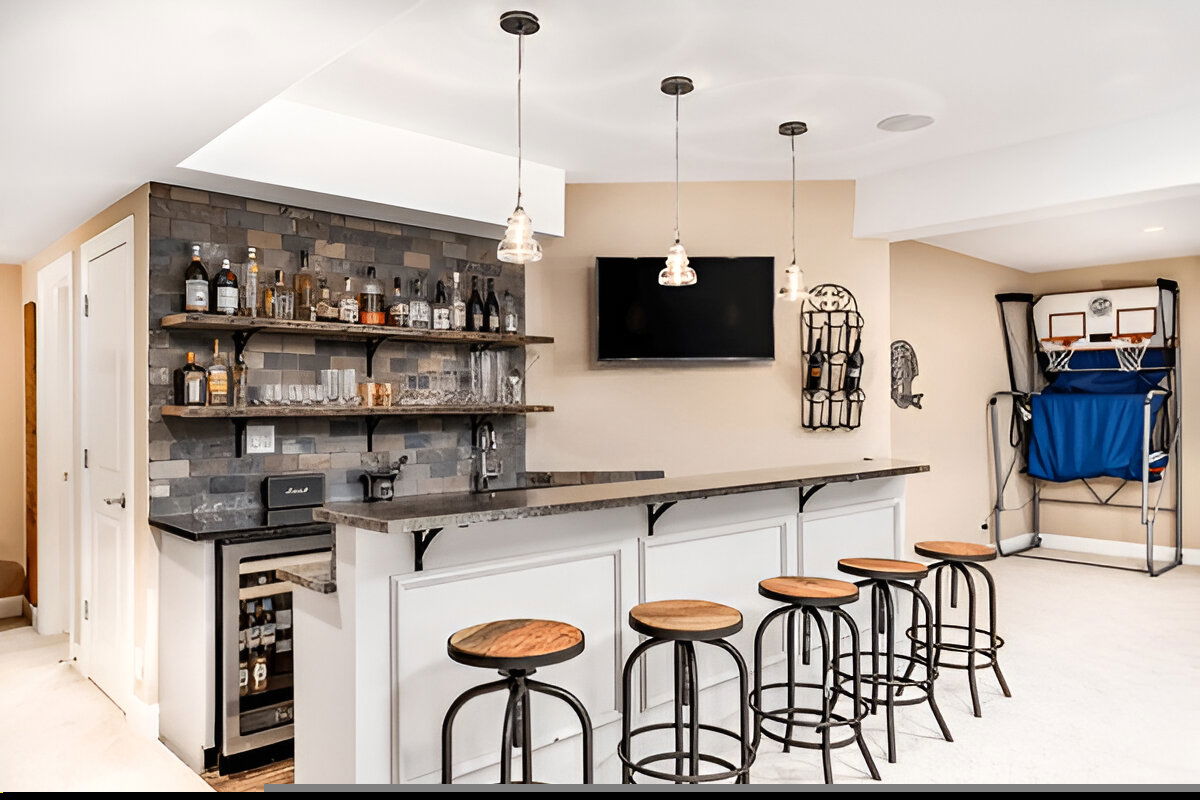 Home bar with rustic wood shelving, gray stone backsplash, pendant lighting, white bar base, and game area with mini basketball hoop.