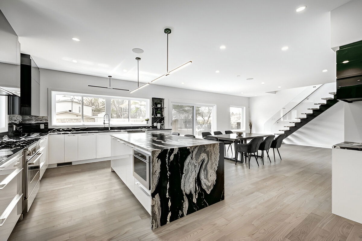 Modern open-concept kitchen with dramatic black and white waterfall island, white cabinets, large windows, and minimalist design.
