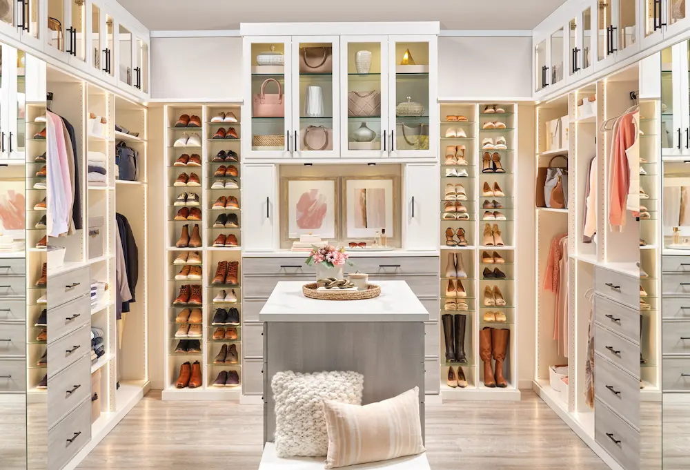 Custom Closets That Elevate Your Space 15 Elegant walk-in closet with built-in shoe storage, glass cabinet doors, hanging space, drawers, center island, and soft lighting.