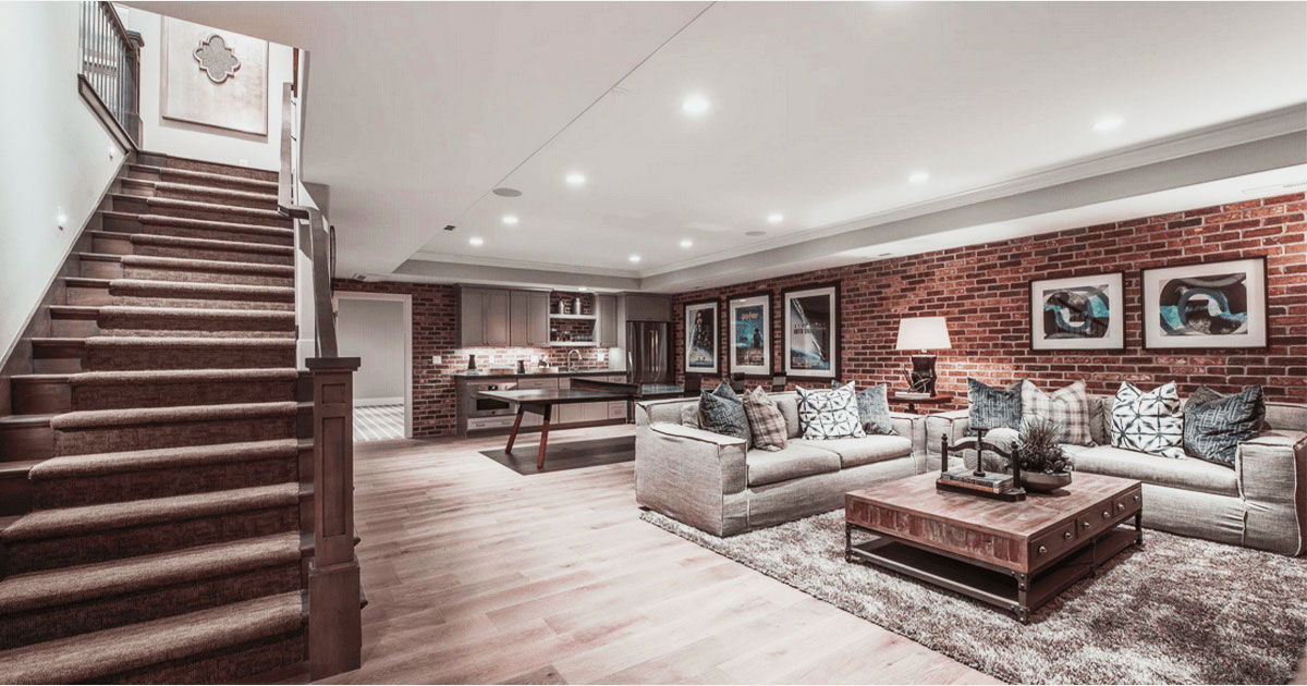 Custom Closets That Elevate Your Space 12 Finished basement with exposed red brick walls, built-in kitchenette, plush seating area, wooden staircase, and cozy lighting.