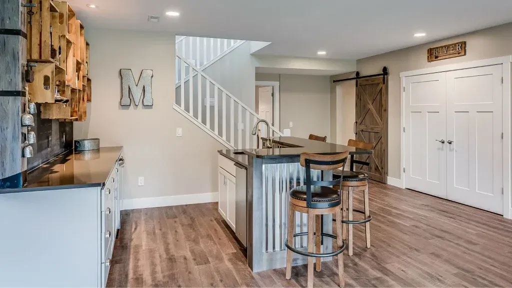 Custom Closets That Elevate Your Space 14 Rustic basement bar with corrugated metal island, wood barstools, barn door, and open shelving on wood flooring.