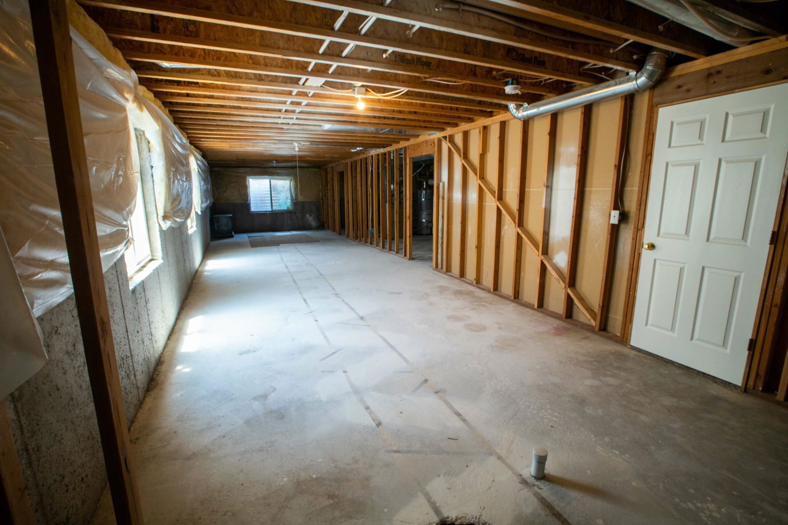 Unfinished basement with exposed wooden framing, concrete floor, visible ductwork, and plastic-covered insulation.