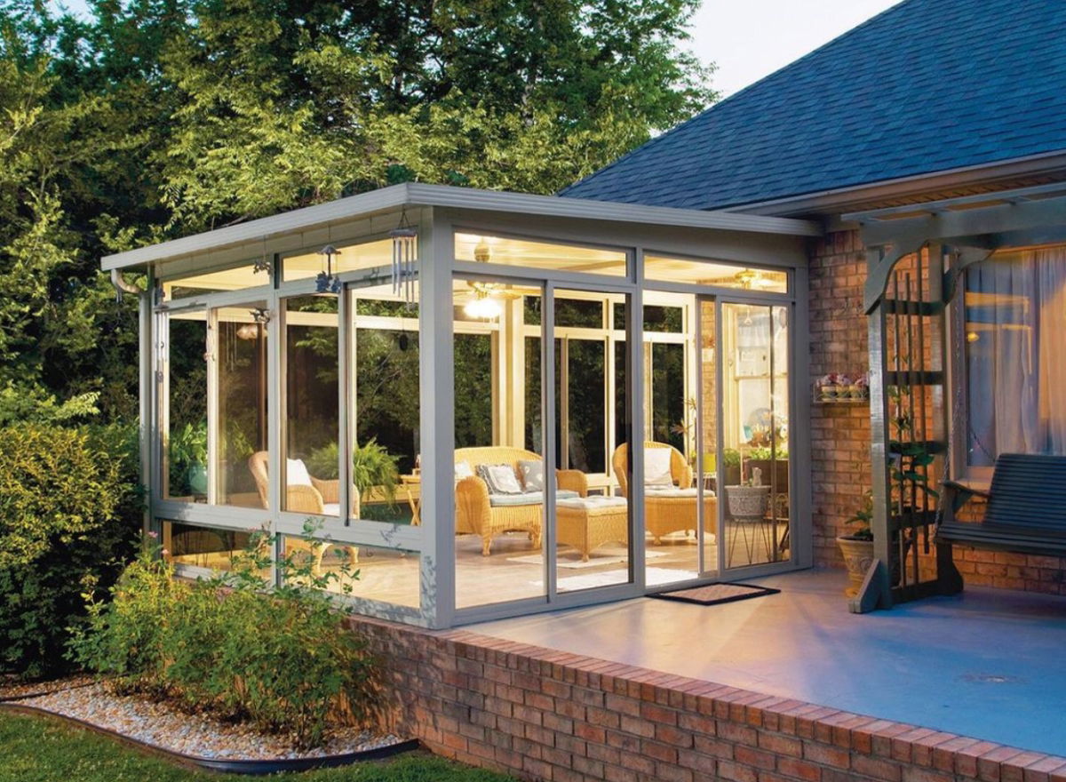 Glass-enclosed sunroom attached to a brick house with cozy wicker furniture 