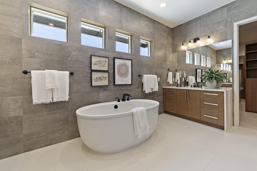 Contemporary bathroom featuring a freestanding bathtub, double sink vanity, wall-mounted decor, and narrow windows