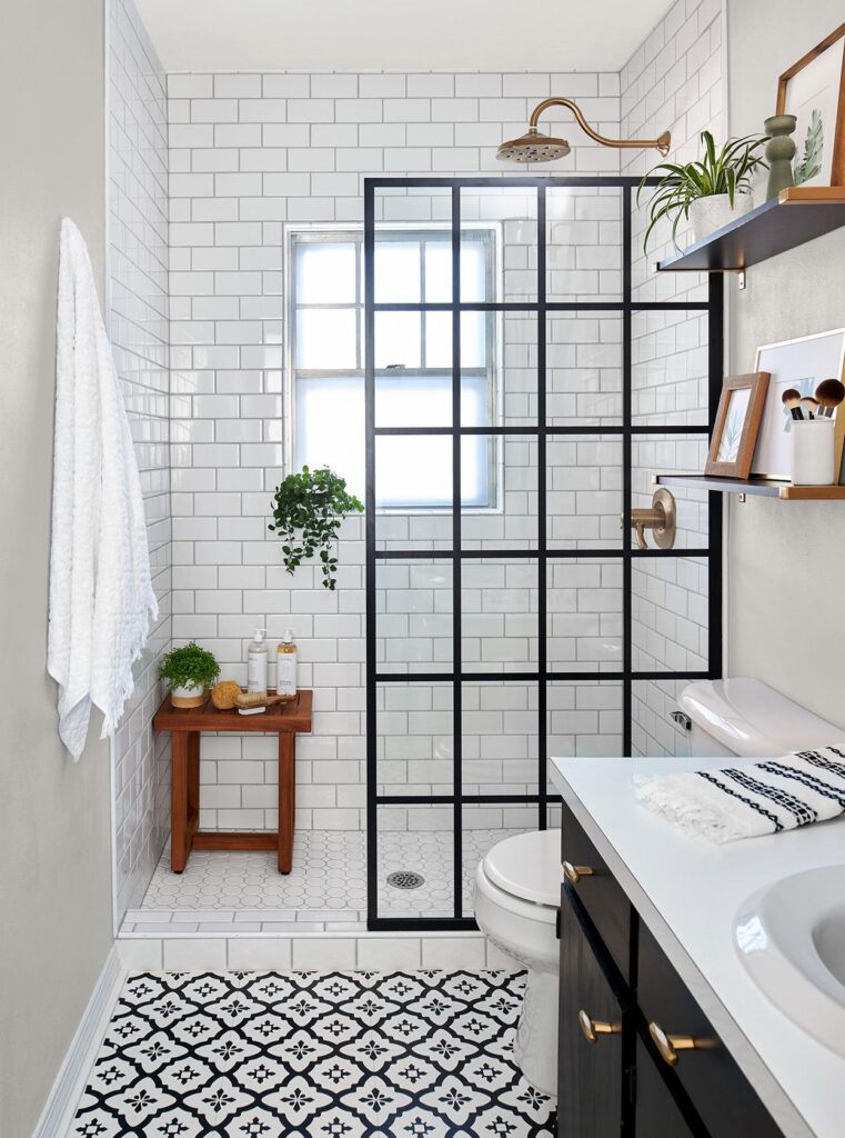 Compact bathroom with black grid shower glass, white subway tiles, patterned floor tiles, and green plants