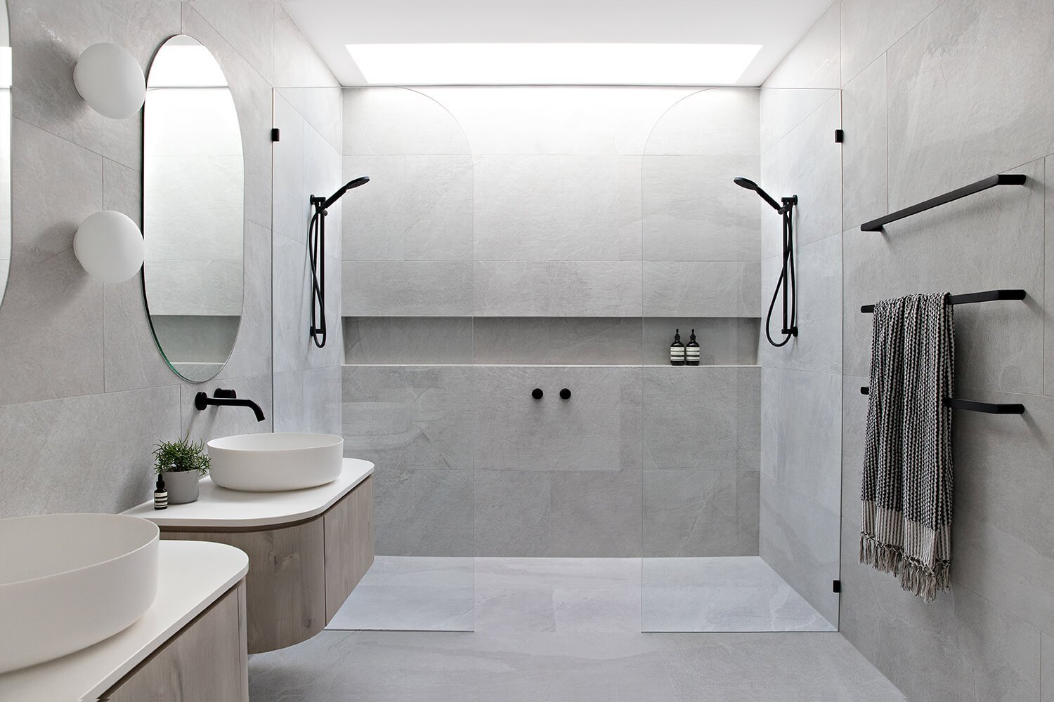 Modern Scandinavian bathroom featuring double walk-in showers, floating vanities, round mirrors, and matte black fixtures