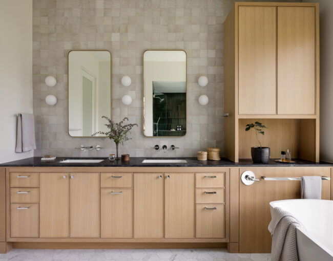 Bathroom featuring light wood cabinetry, black countertops, dual rectangular mirrors, and soft tile backsplash