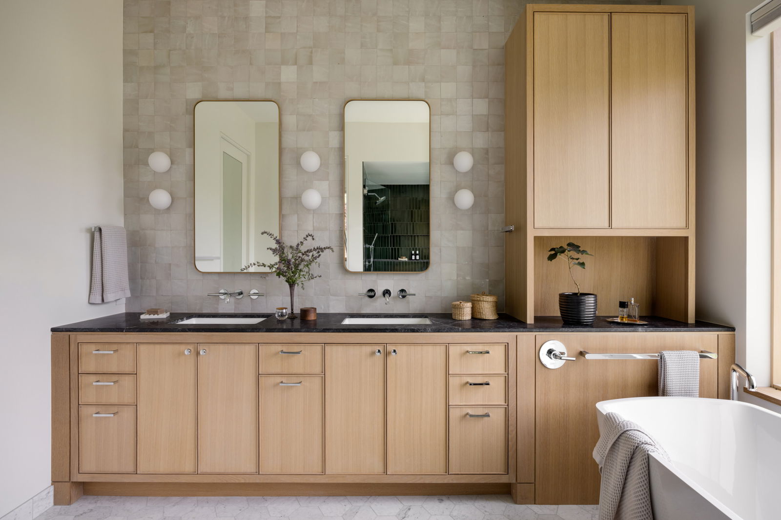 Bathroom featuring light wood cabinetry, black countertops, dual rectangular mirrors, and soft tile backsplash