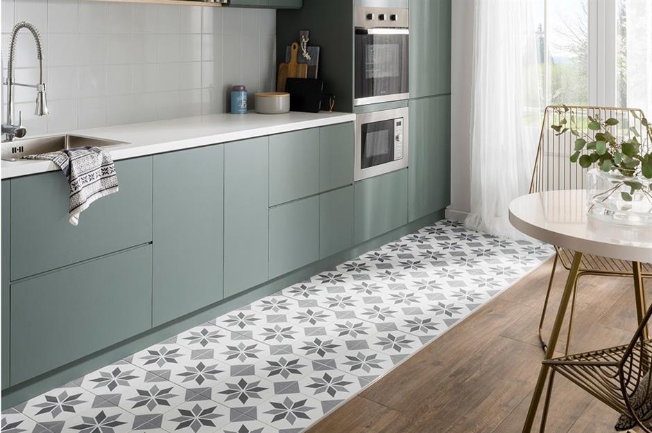 Modern kitchen featuring muted green cabinetry, white countertops, and a decorative patterned tile floor section creating a zoning effect within the wood floor layout.