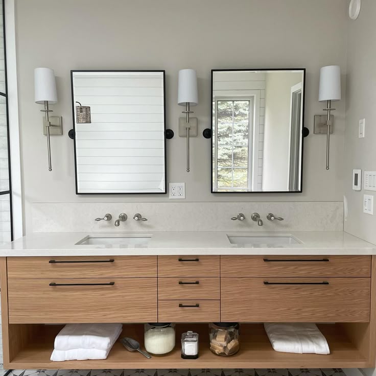 Contemporary bathroom double vanity featuring light wood drawers, black hardware, wall-mounted faucets, and dual mirrors