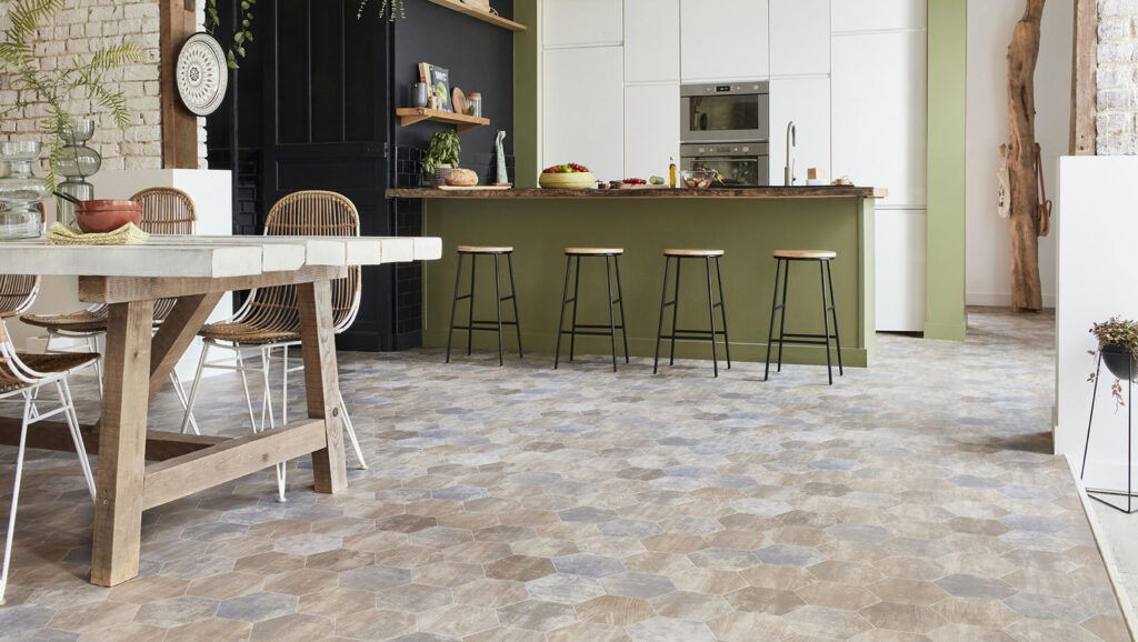 Open-plan kitchen with natural wood dining table, rattan chairs, and multi-toned hexagon tile flooring.