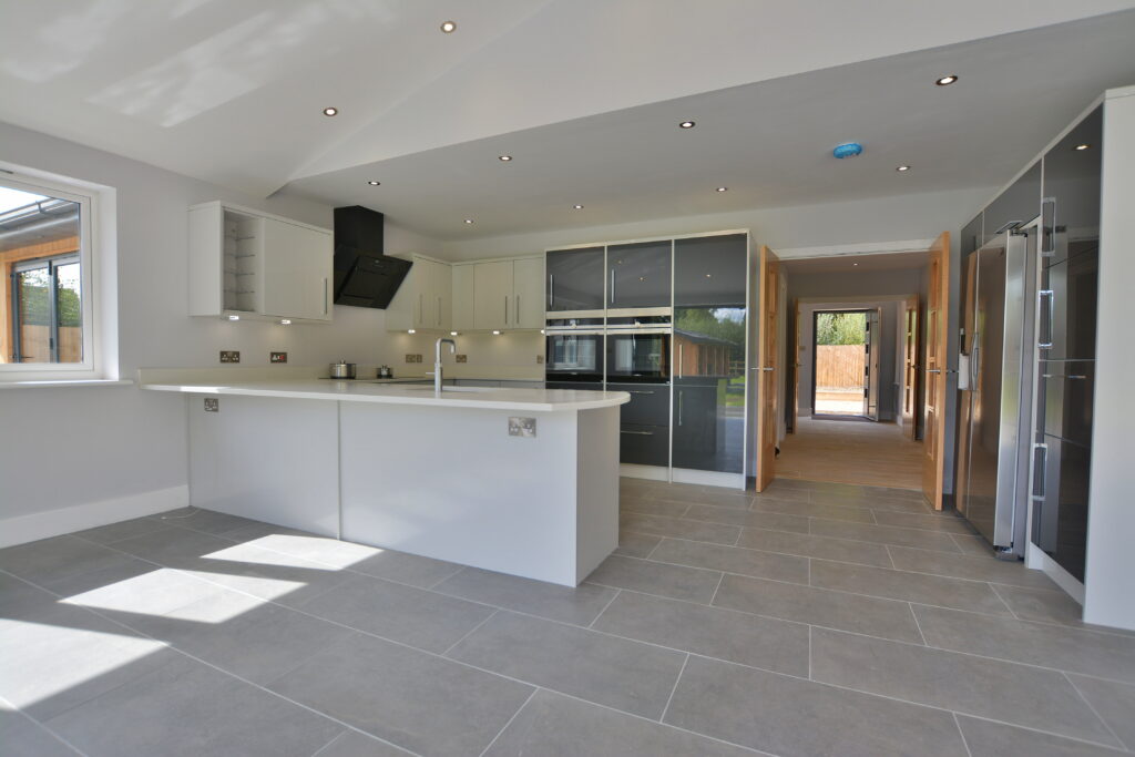 Contemporary kitchen featuring large grey ceramic floor tiles, sleek white island, built-in appliances, and glossy cabinets