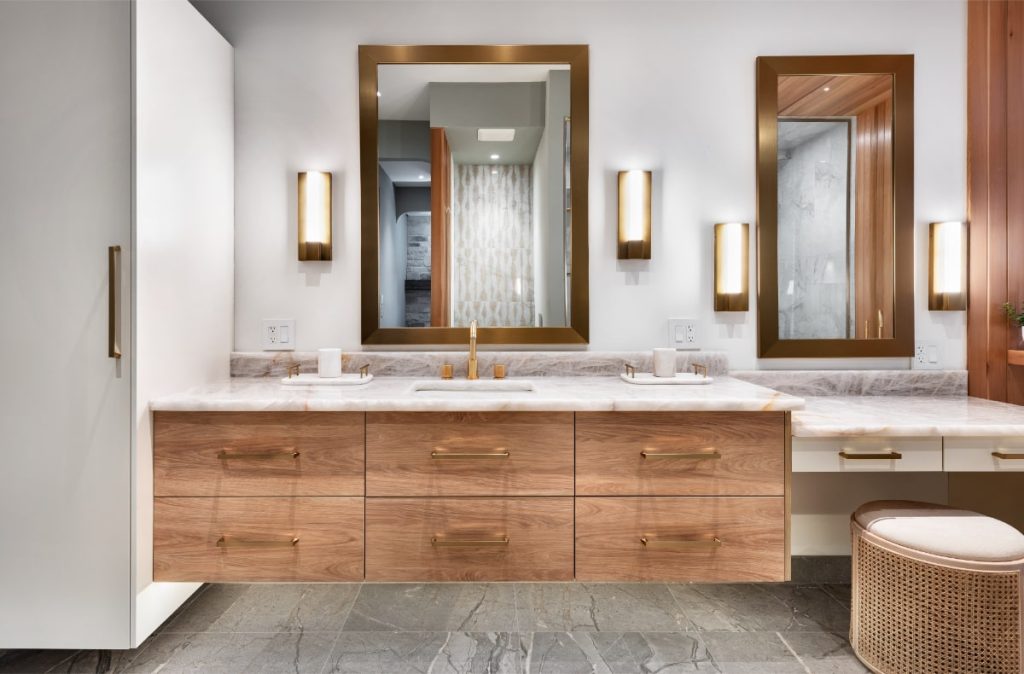 Contemporary bathroom with a floating wood vanity, marble countertop, brass-framed mirrors, and soft wall lighting.