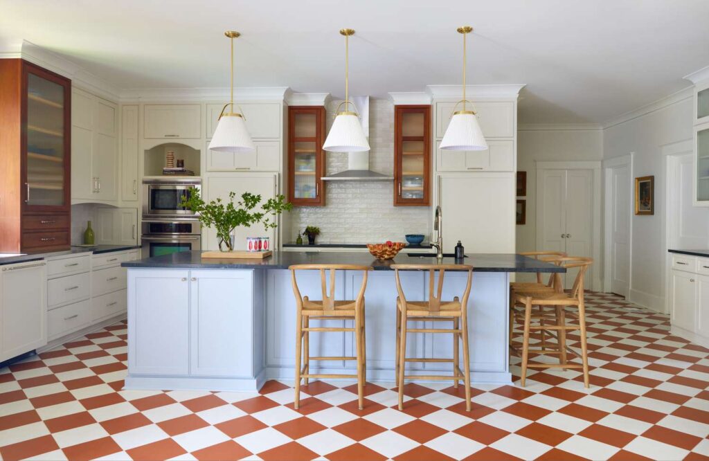 A classic kitchen featuring red and white checkered tile flooring, a large central island with wooden bar stools, and white cabinetry with modern pendant lighting.