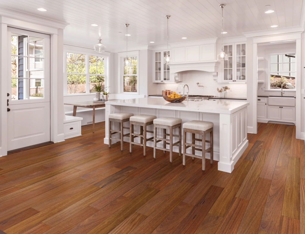 Modern kitchen with teak engineered wood flooring, white cabinetry, and a central island with bar stools