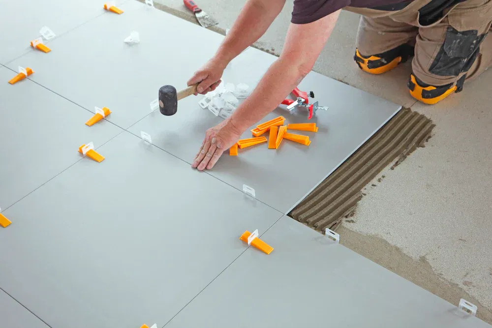 Contractor installing large floor tiles using tile leveling clips and mortar for even surface alignment