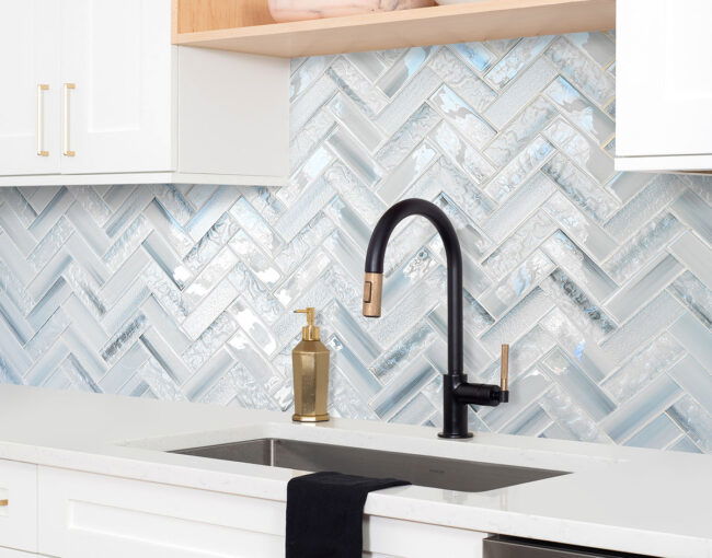 Contemporary white kitchen with blue glass herringbone backsplash, black matte faucet, and quartz countertop