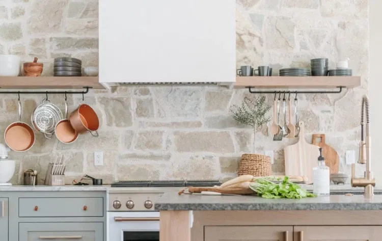 Rustic kitchen design featuring a natural stone backsplash, open wooden shelves, and copper cookware