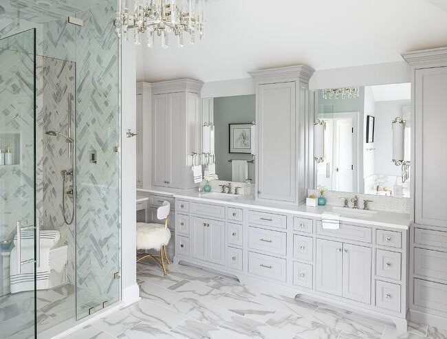 Luxurious master bathroom with gray cabinetry, marble tile floors, built-in vanity space, and a frameless glass shower enclosure.