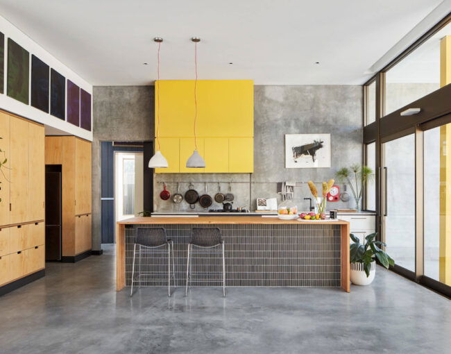 Contemporary kitchen with concrete floors, yellow upper cabinets, wood accents, and large glass doors
