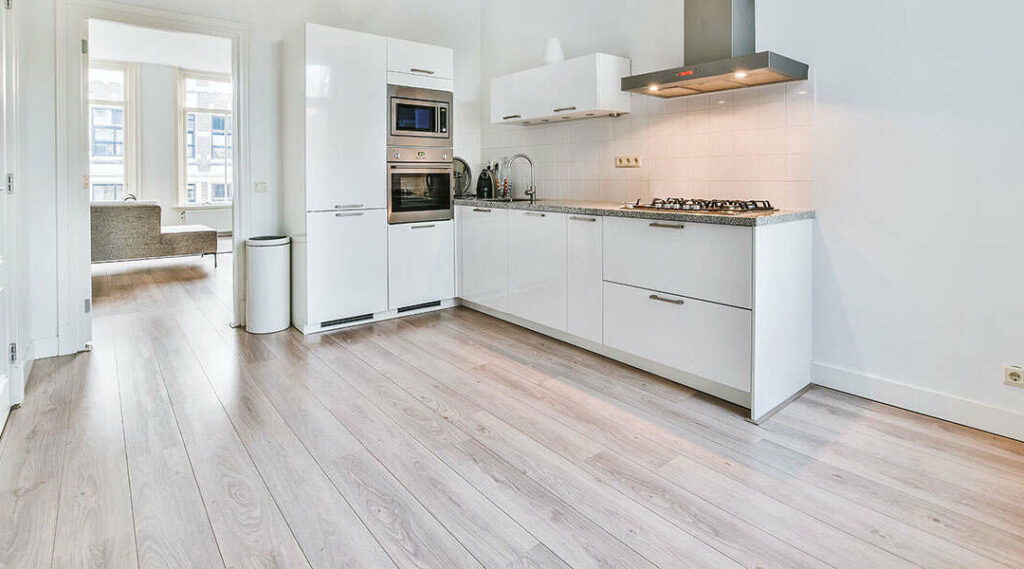Minimalist kitchen with white cabinets, stainless steel appliances, and light laminate wood flooring
