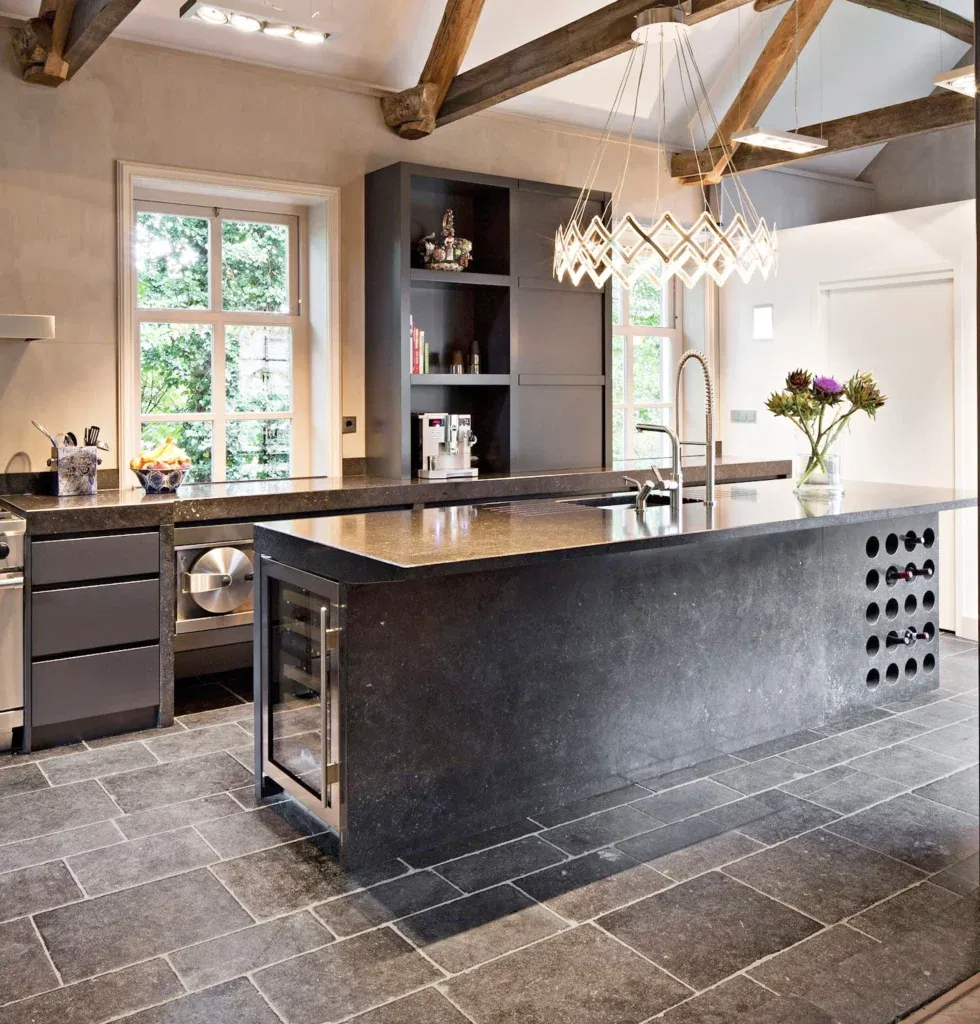 Rustic modern kitchen featuring natural stone tile flooring, exposed wooden beams, and a sleek black island with wine storage