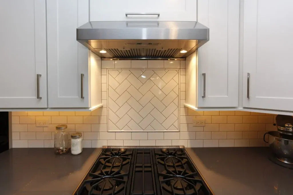 Modern white kitchen with a classic subway tile backsplash featuring a herringbone pattern focal point behind a stainless steel range hood