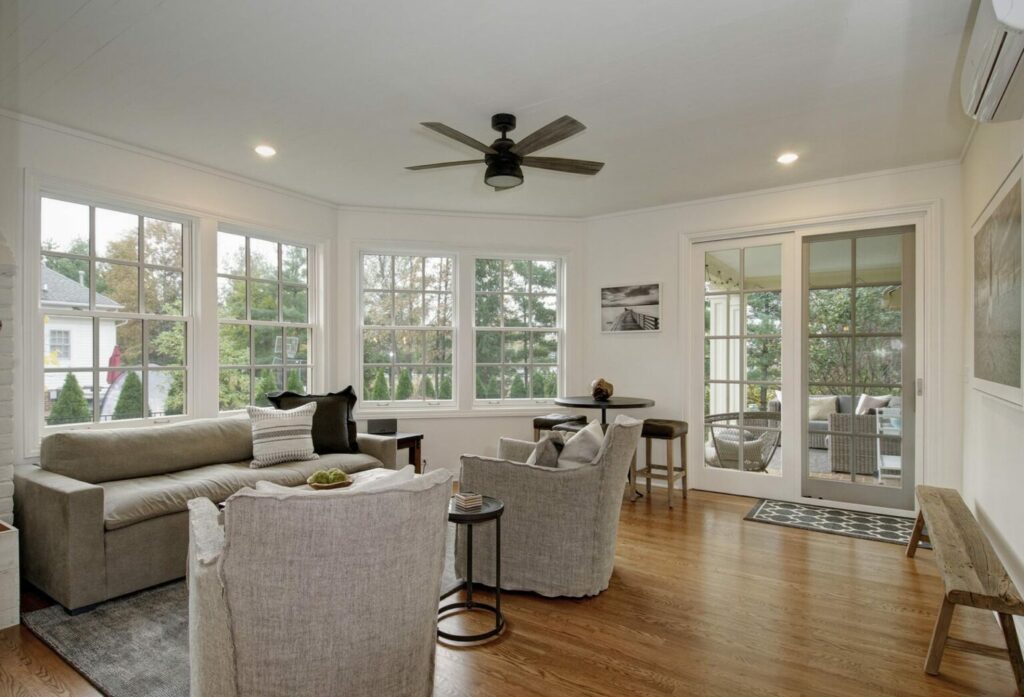 Bright sunroom addition with large windows, neutral furnishings, and hardwood flooring.