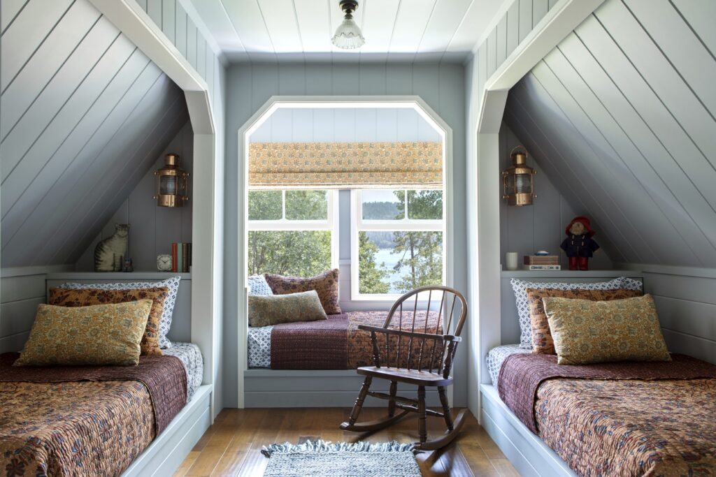 Cozy attic bedroom with twin beds, a window seat, and a wooden rocking chair.