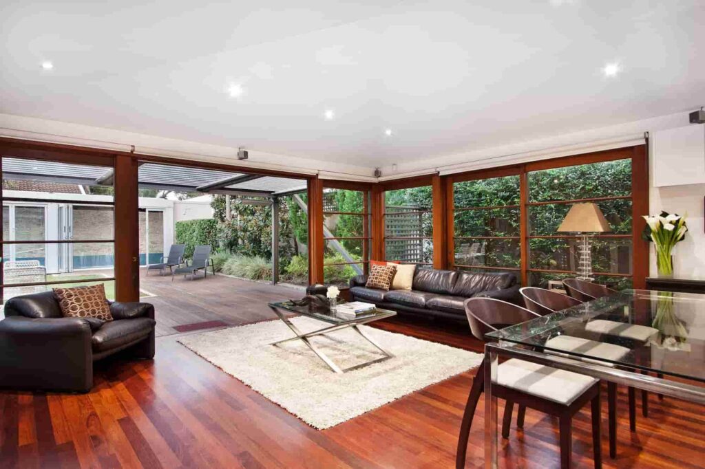 Modern living room with glass walls opening to a wooden patio and garden.