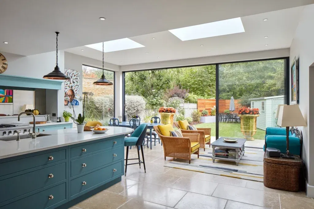 Bright kitchen extension with skylights, blue cabinetry, and large glass doors opening to a colorful garden.